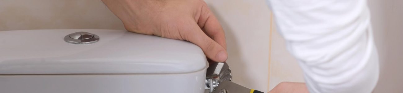 Naprawa cieknącej spłuczki. Ręce fachowca, w których trzyma kombinerki dotykają do spłuczki.