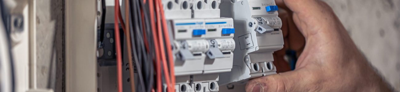 A male electrician works in a switchboard with an electrical connecting cable, connects the equipment with tools.