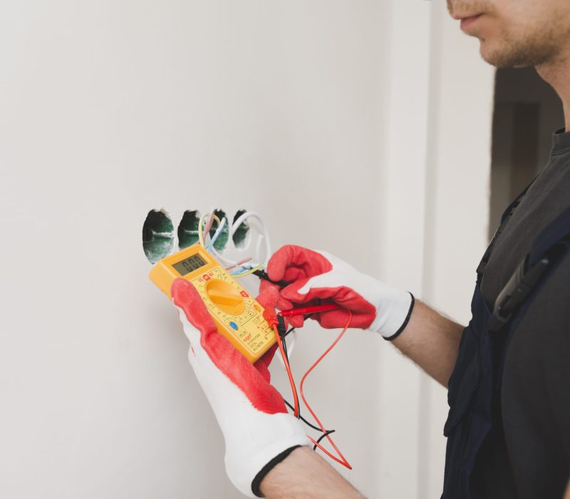 Specjalista wykonujący naprawę instalacji elektrycznej w domu. Zwisające kable z dziury po gniazdku i zbliżenie na ręcę, które wszystko składają.
